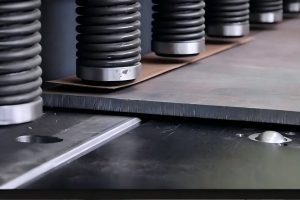 Row of bellow-protected hold-down cylinders clamping a steel sheet on a hydraulic shearing machine