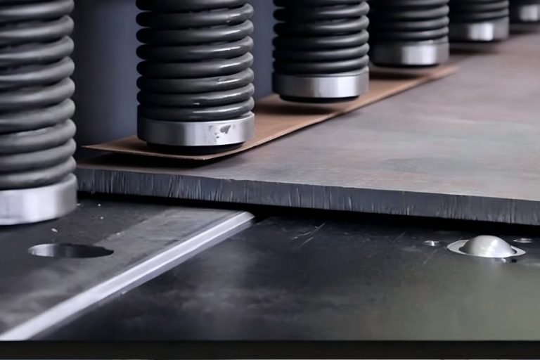 Row of bellow-protected hold-down cylinders clamping a steel sheet on a hydraulic shearing machine